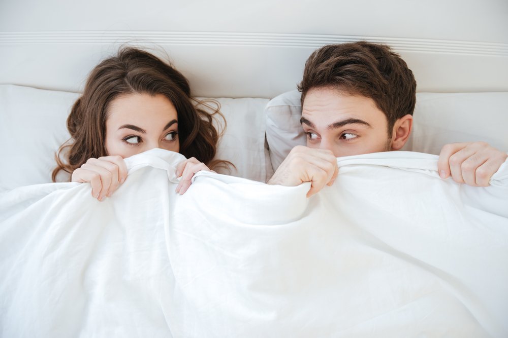 Funny young couple lying and hiding under the blanket