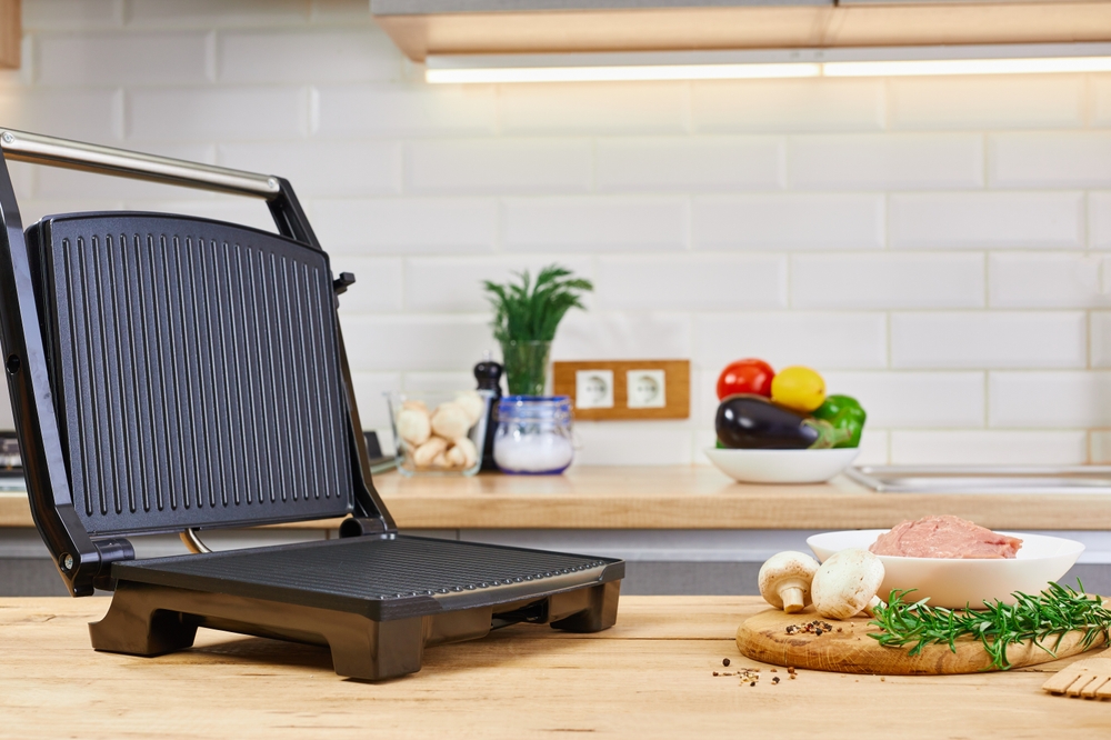 Electric grill with meat and spices on cutting board