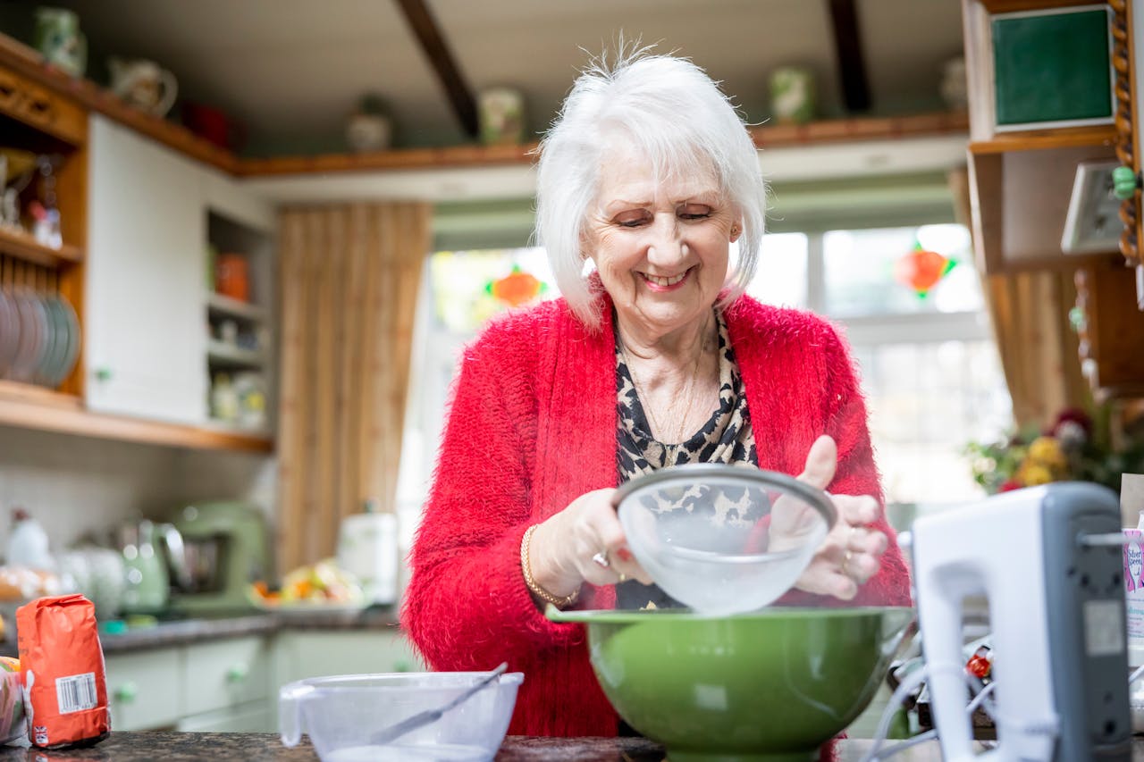 Elderly Woman in a Red Cardigan Sifting Flour