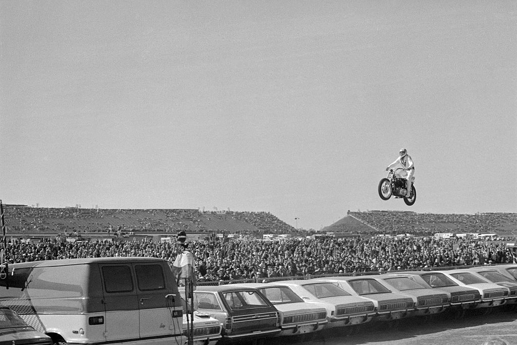Motorcycle stunt man Evel Knievel sails over a line of 19 automobiles