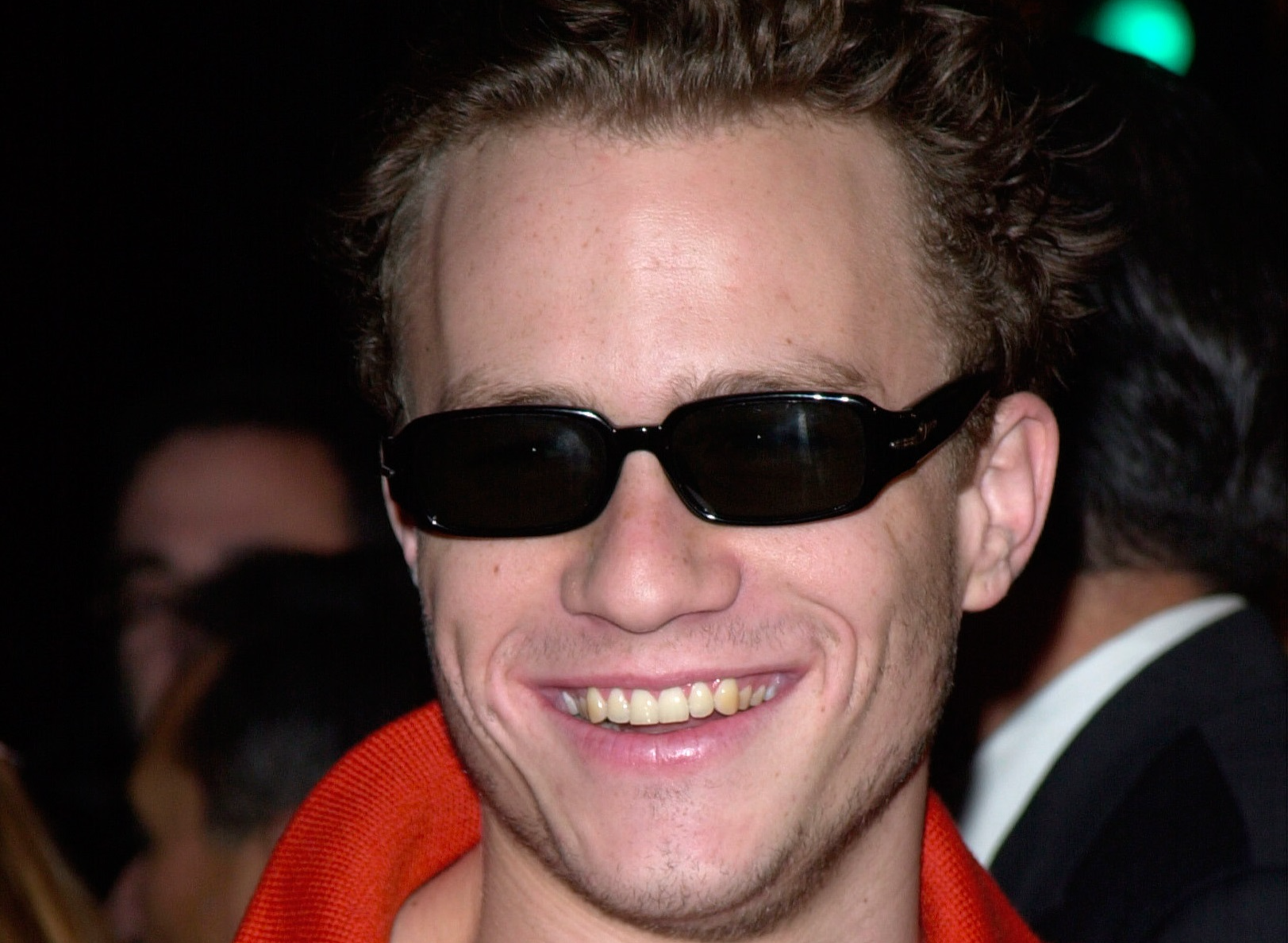 Heath Ledger with glasses wearing red jacket and smiling to the camera - 2001