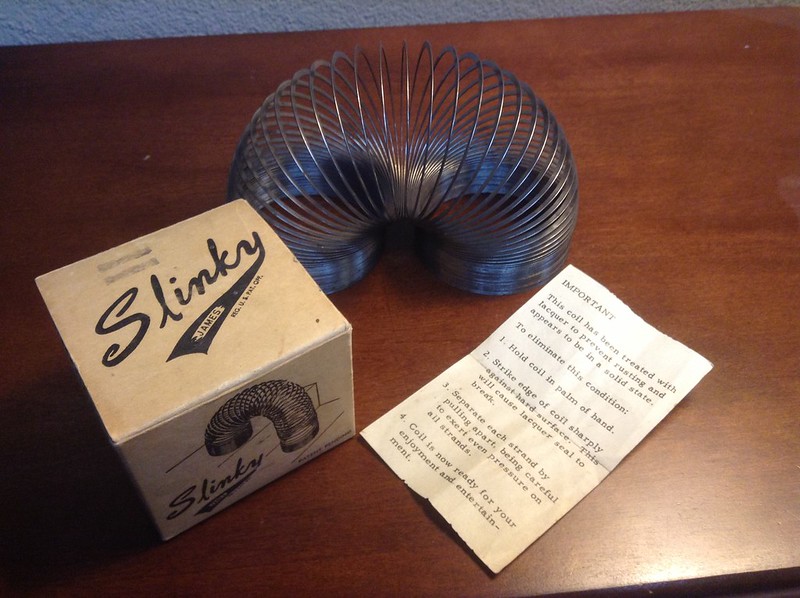The image shows a vintage Slinky toy and its original packaging