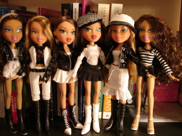 A group of five Bratz dolls are lined up against a bookshelf