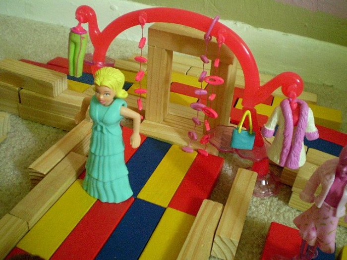 A blonde Polly Pocket doll wearing a teal dress stands on a platform made of colorful blocks
