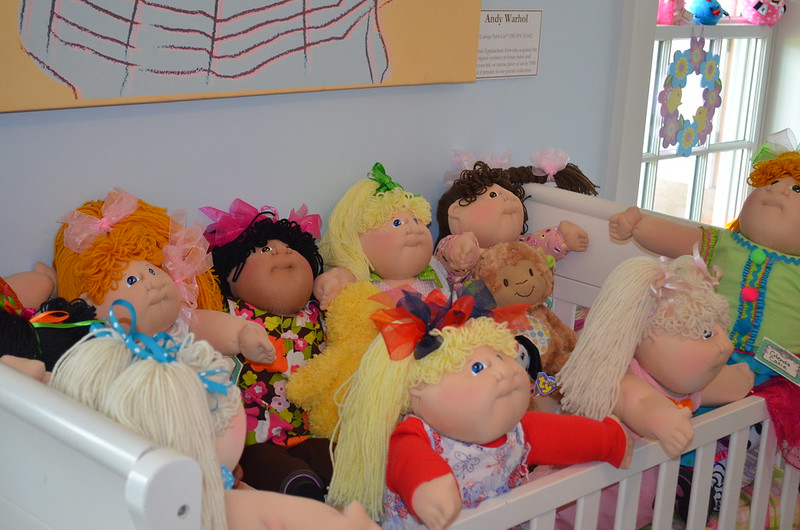 A group of Cabbage Patch Kids dolls are gathered in a crib, looking like a happy family.