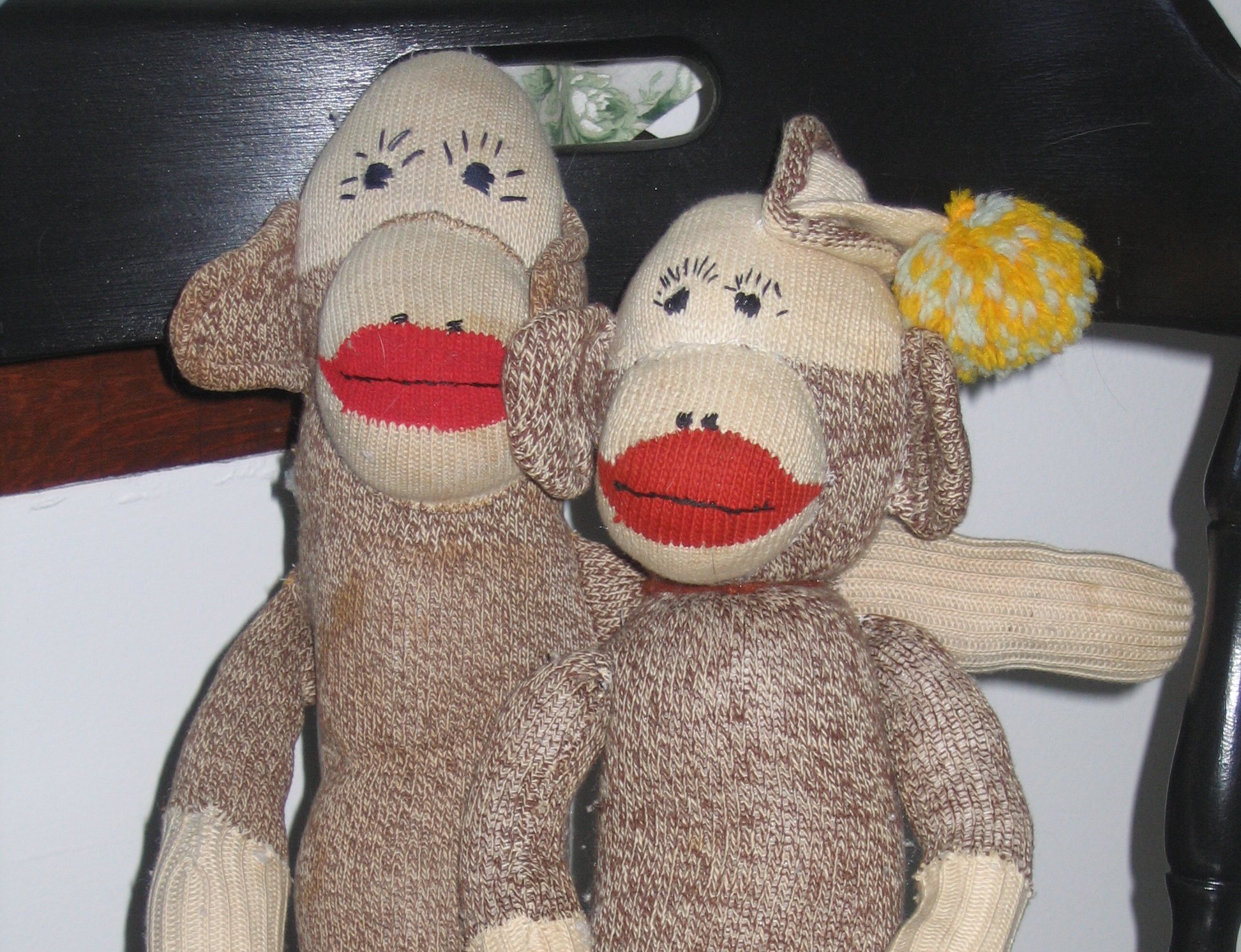 The image shows two sock monkeys sitting on a wooden chair.