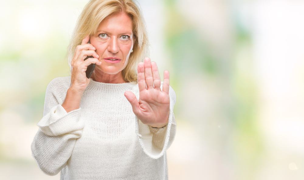 Middle age blonde woman talking on smartphone stopping someone
