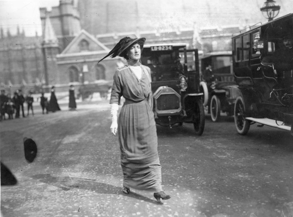 Margot Asquith in dress and a hat in front of a car