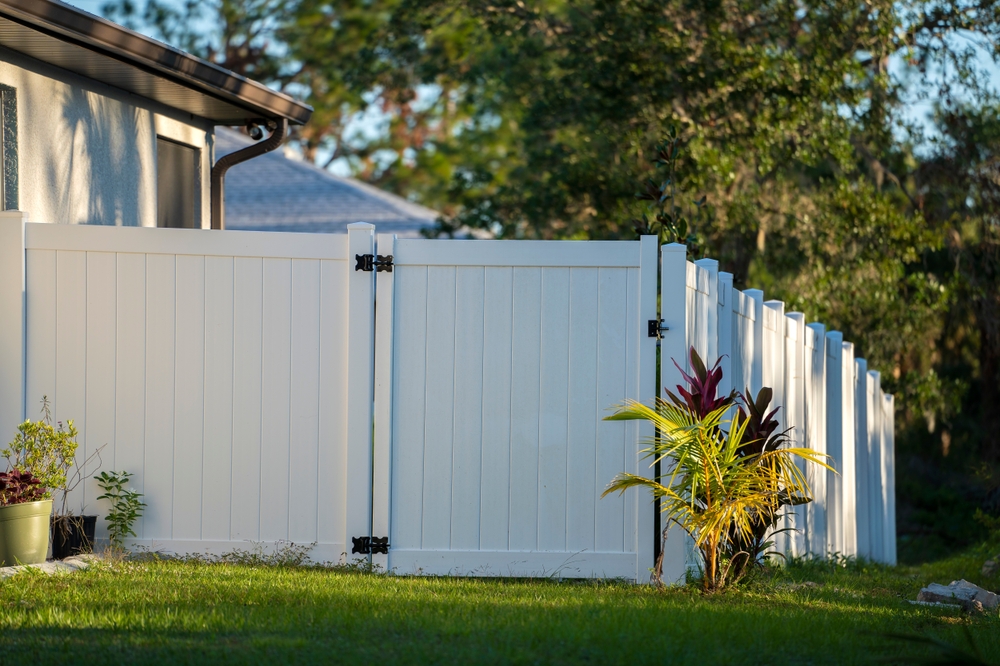 White vinyl picket fence on green lawn surrounding property grounds for backyard protection and privacy