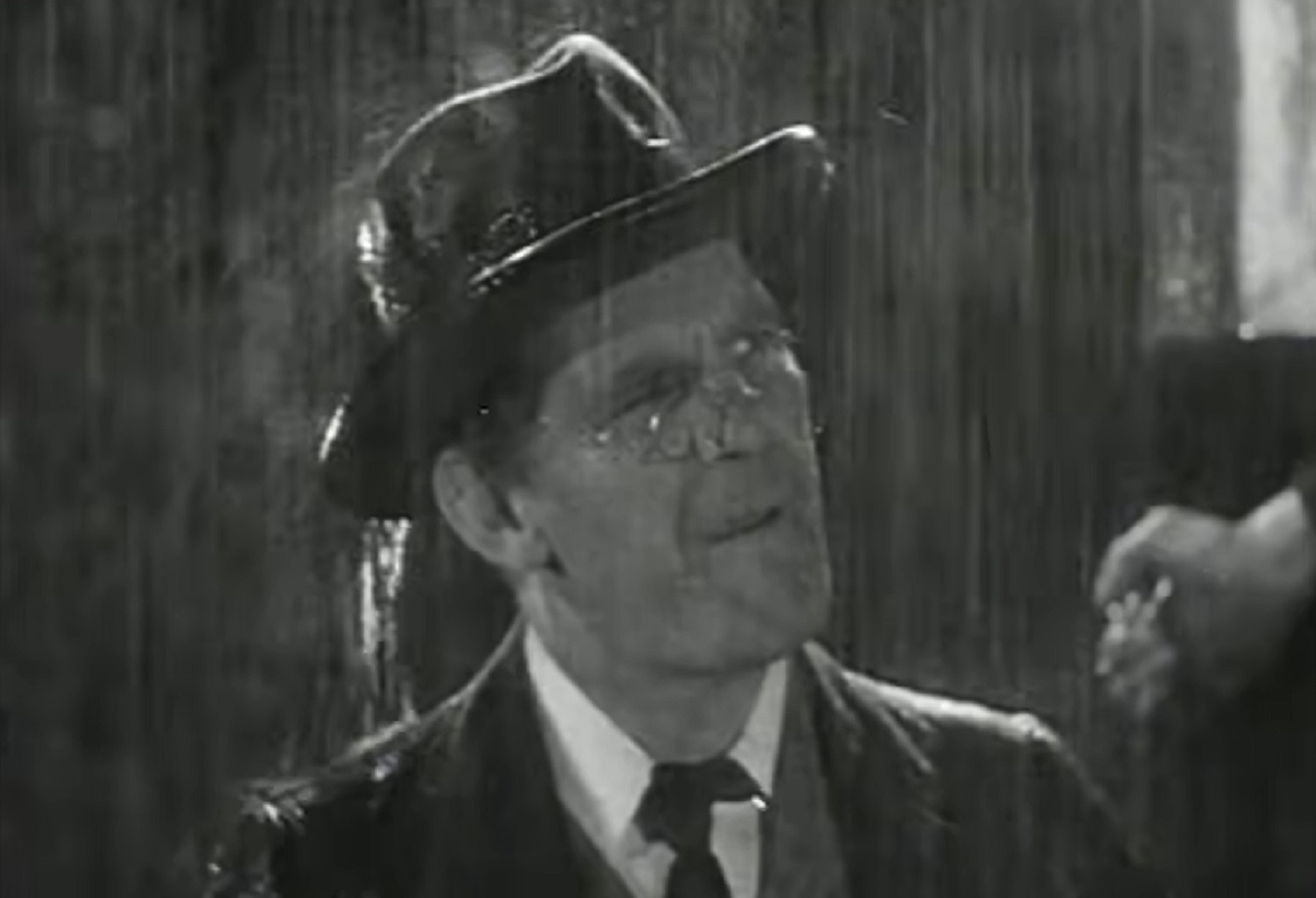 Screenshot of Will Hay standing on the rain outside - from Oh, Mr Porter! (1937)