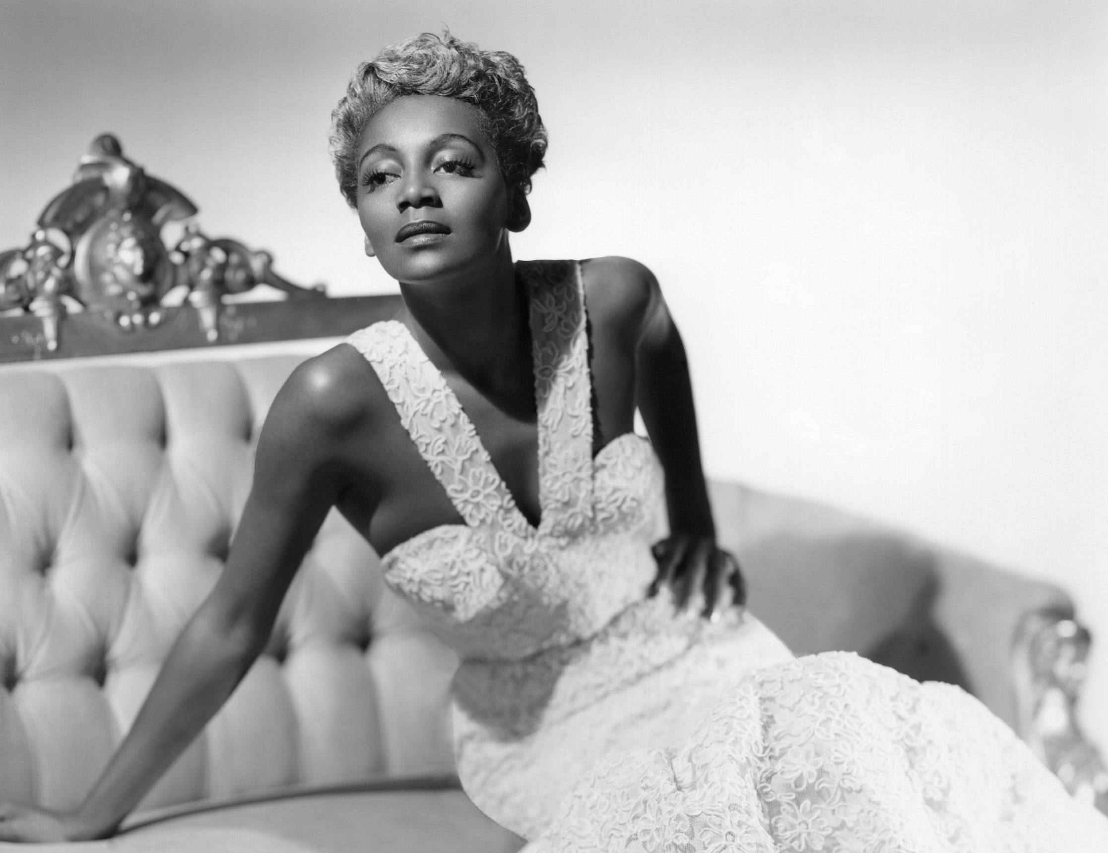 Actress and Singer Joyce Bryant lounges on a sofa with her signature silver hair and mermaid dress - 1953
