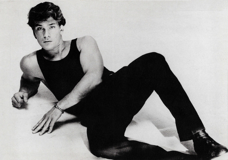 Grayscale photo of actor Patrick Swayze wearing a black outfit and lying on the floor