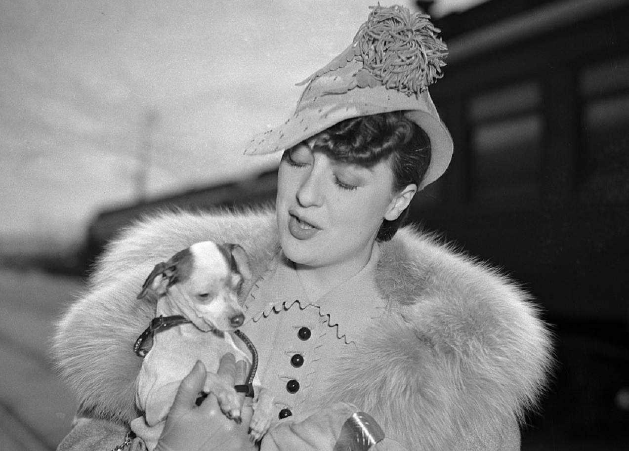 Portrait of Gypsy Rose Lee carrying dog at train station, circa 1937