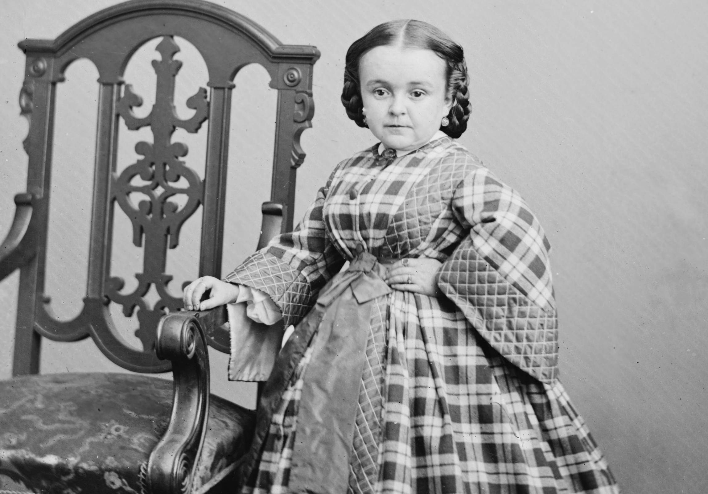 Lavinia Warren in plaid dress next to a chair