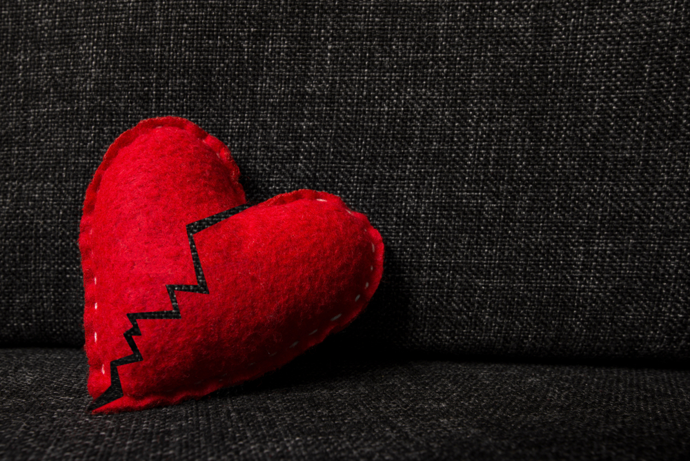 Broken red valentines day heart made from wool on dark fabric background
