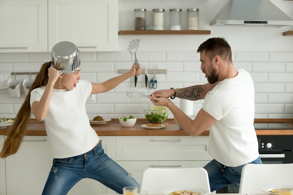Funny couple pretending fight with utensils tools while cooking