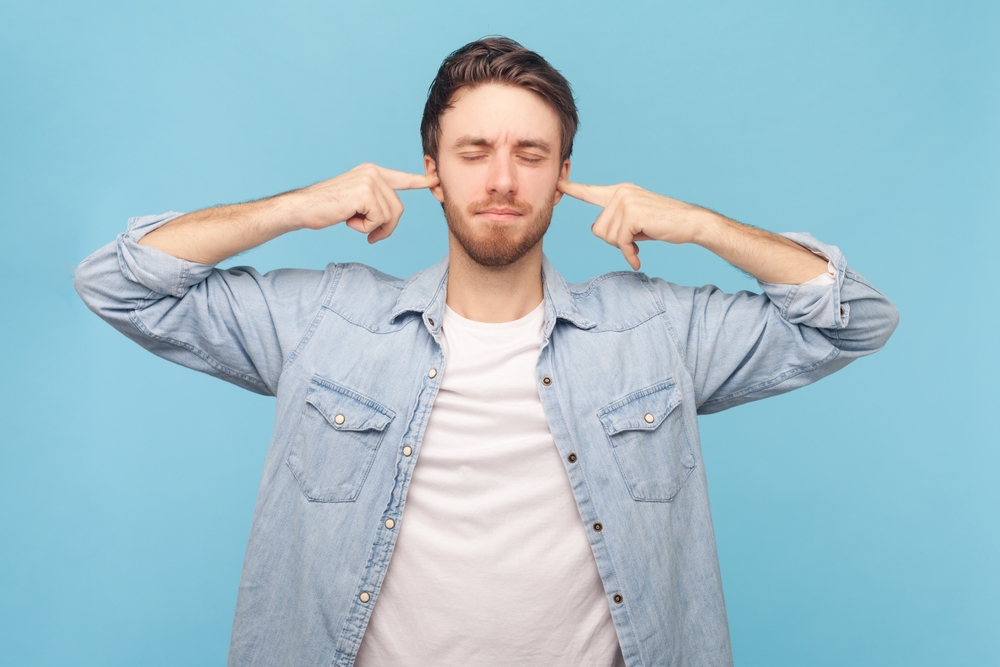 man closing eyes and plugging ears with fingers