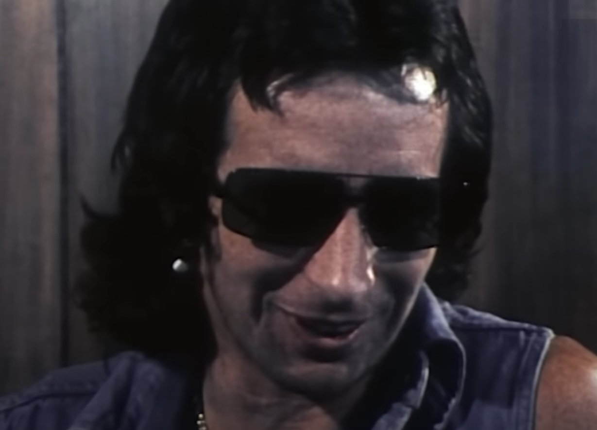 Screenshot of Bonn Scott smiling at camera from - On The Brink (2022)