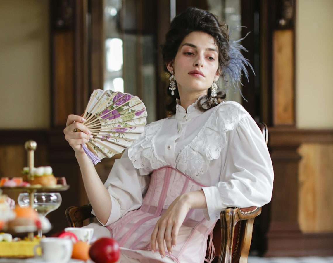 A Woman in a White Long Dress with Corset Holding a Hand Fan