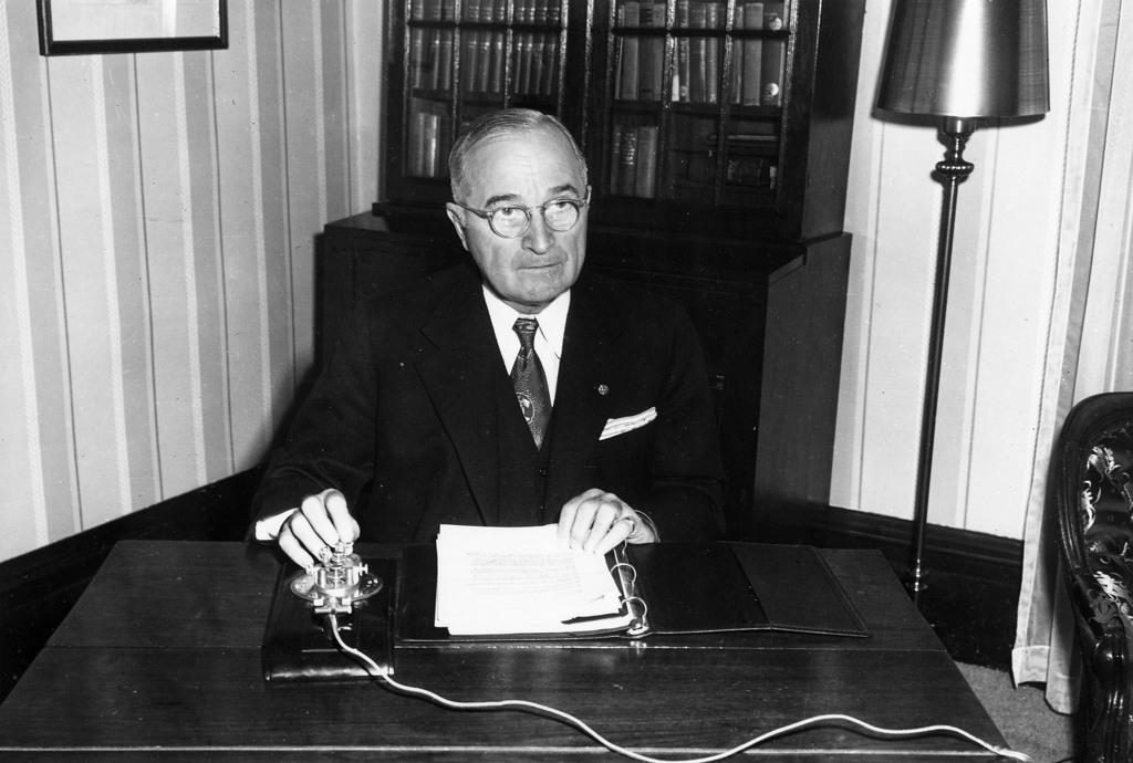 President Harry S. Truman in a suit sitting at this desk