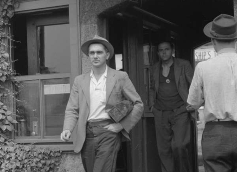 A man in a suit and hat walking out of a building