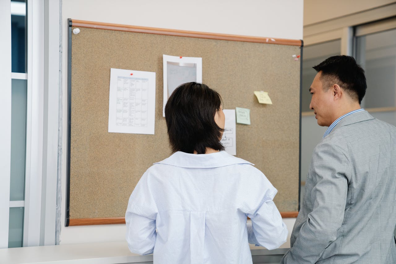 Man and a Woman Talking in Front of a Bulletin Board
