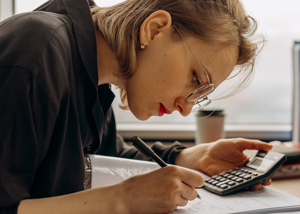 A Woman Writing on a Book while Holding a Calculator