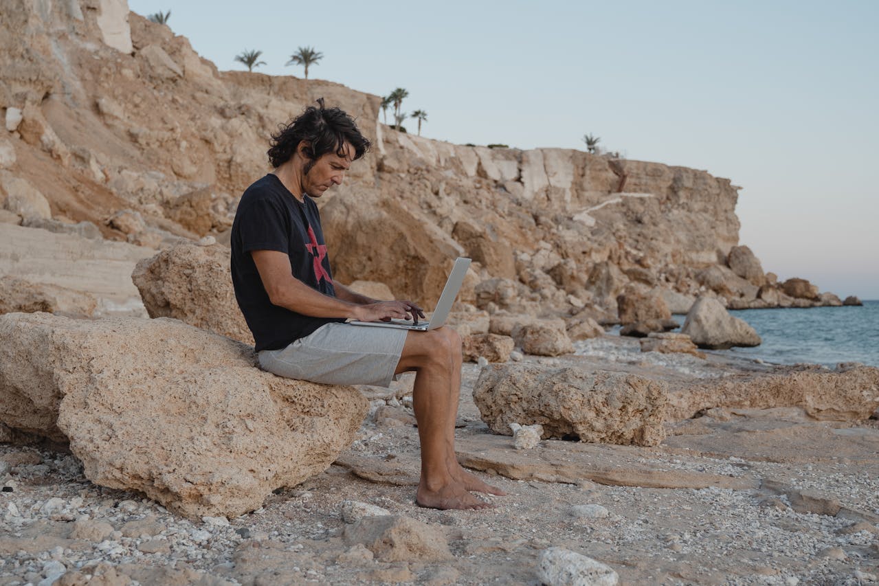 Man Sitting on the beach and Using a Laptop