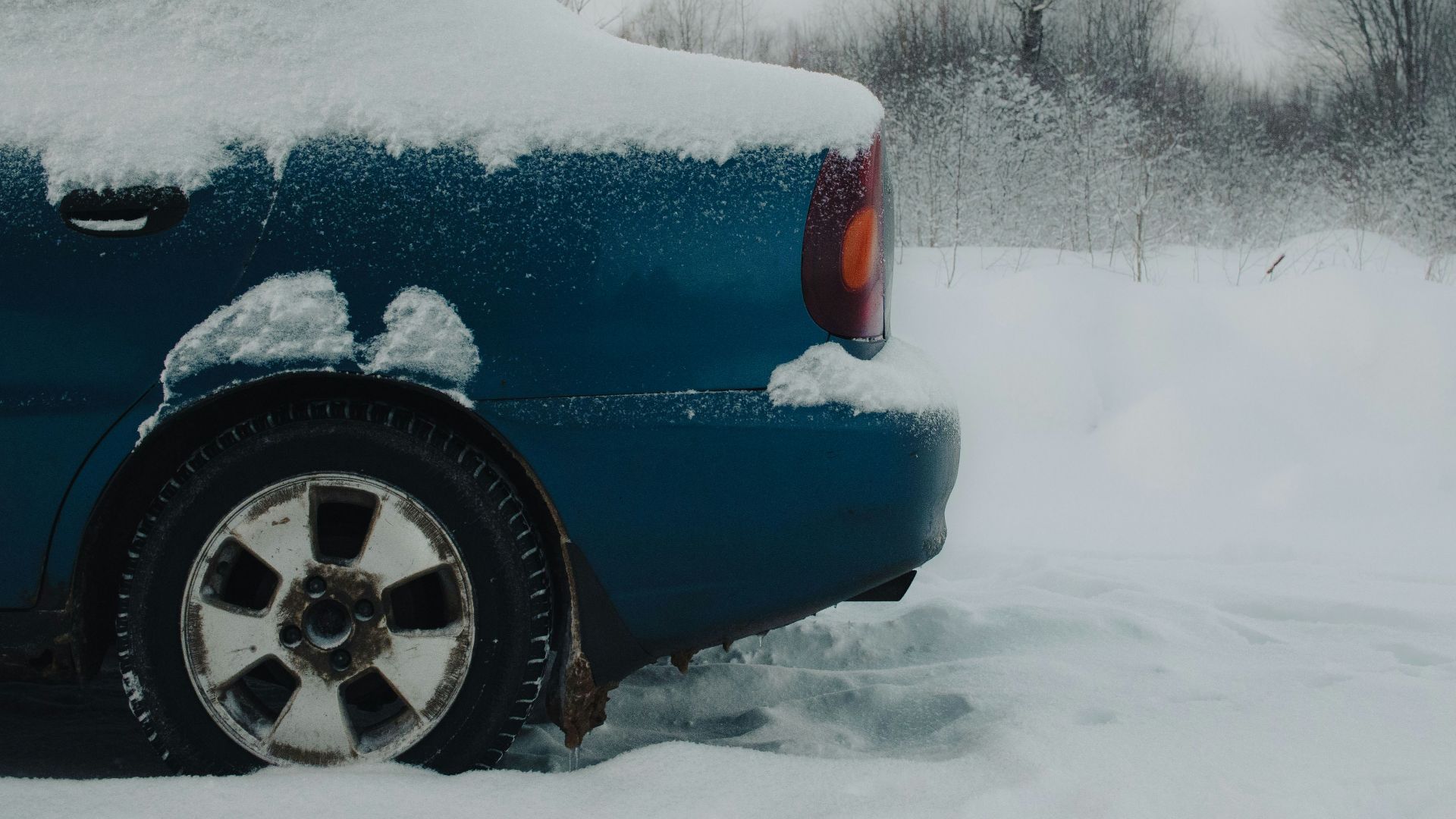 a blue car covered in snow on a snowy day