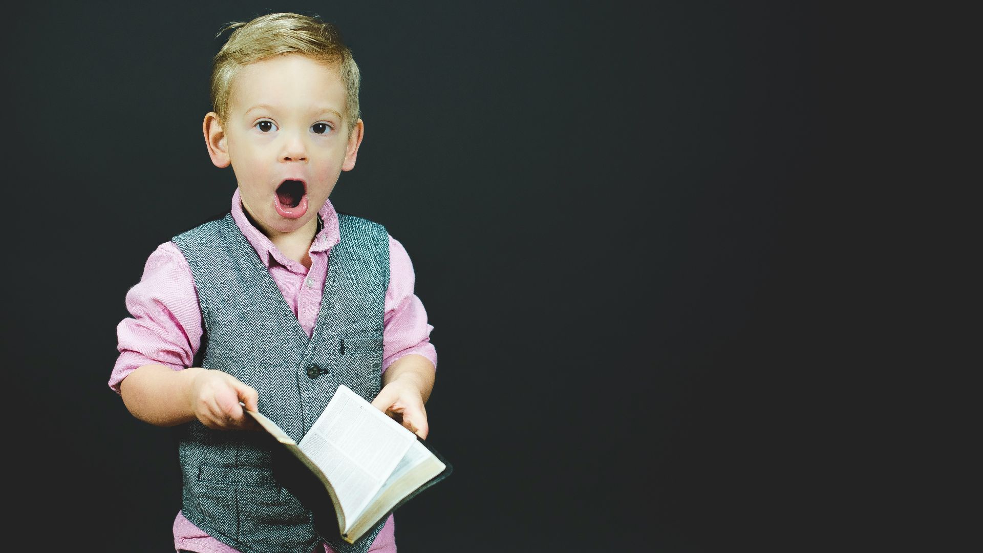 boy wearing gray vest and pink dress shirt holding book