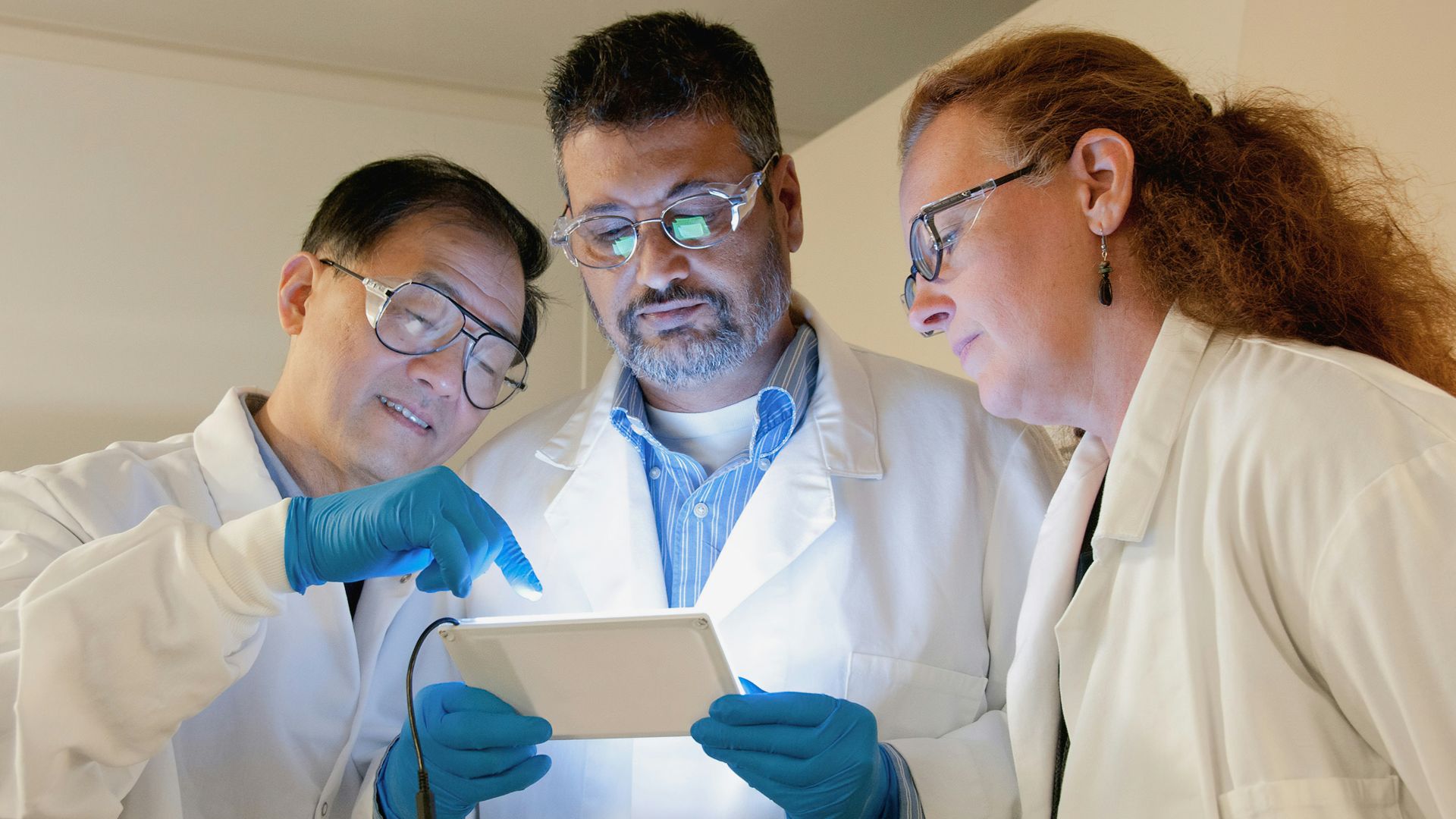 three people in lab coats looking at a tablet