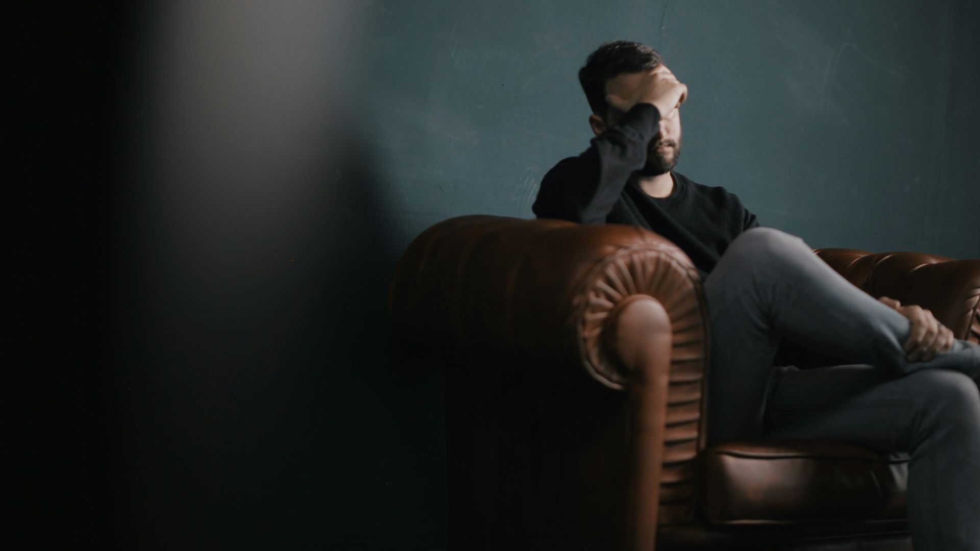 a man holds his head while sitting on a sofa