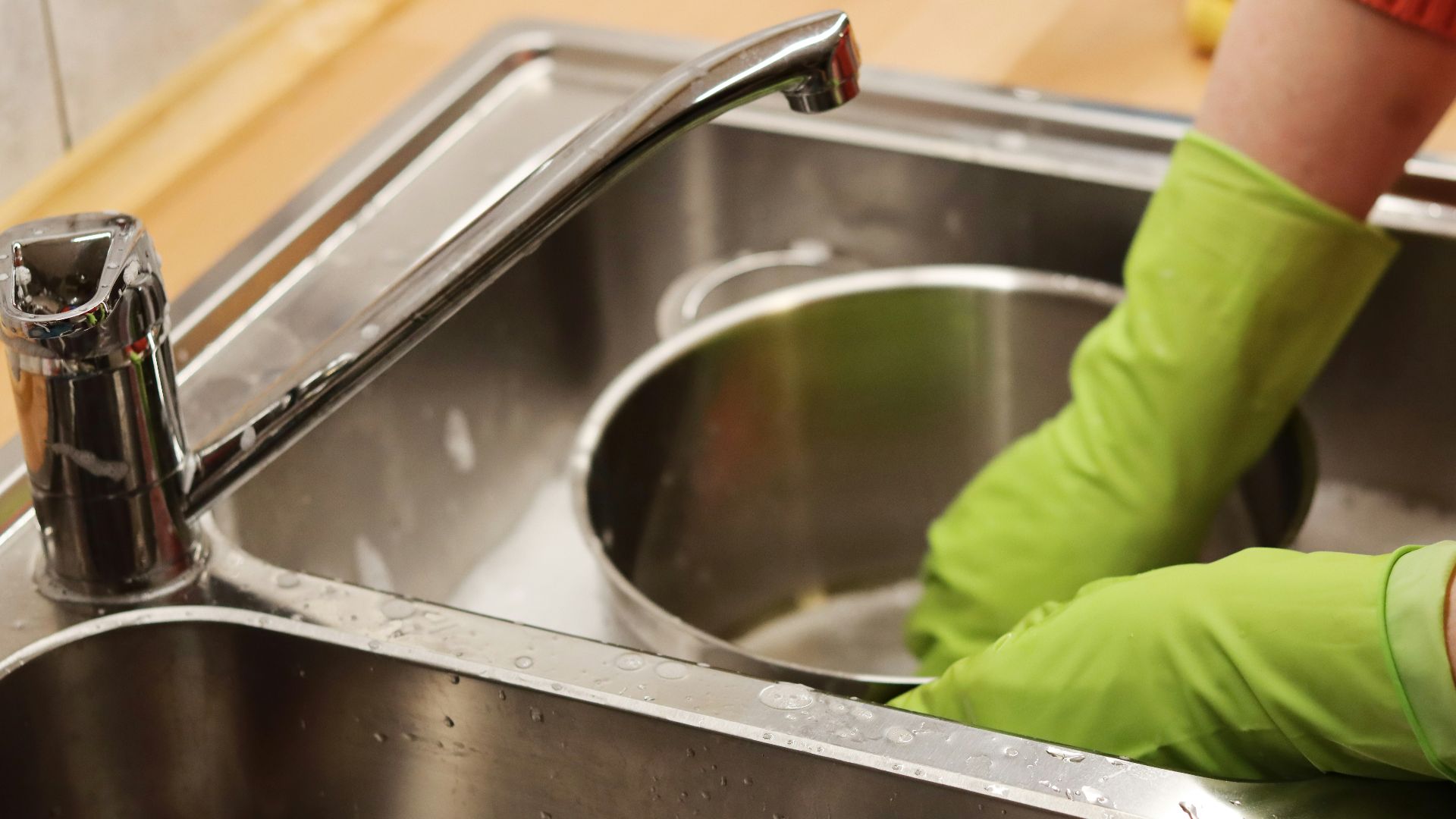 person in green long sleeve shirt washing stainless steel sink