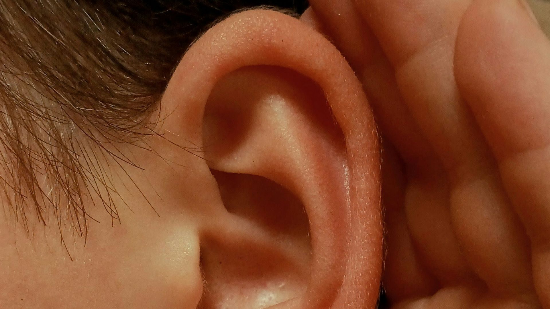 A person cupping their ear to listen closely