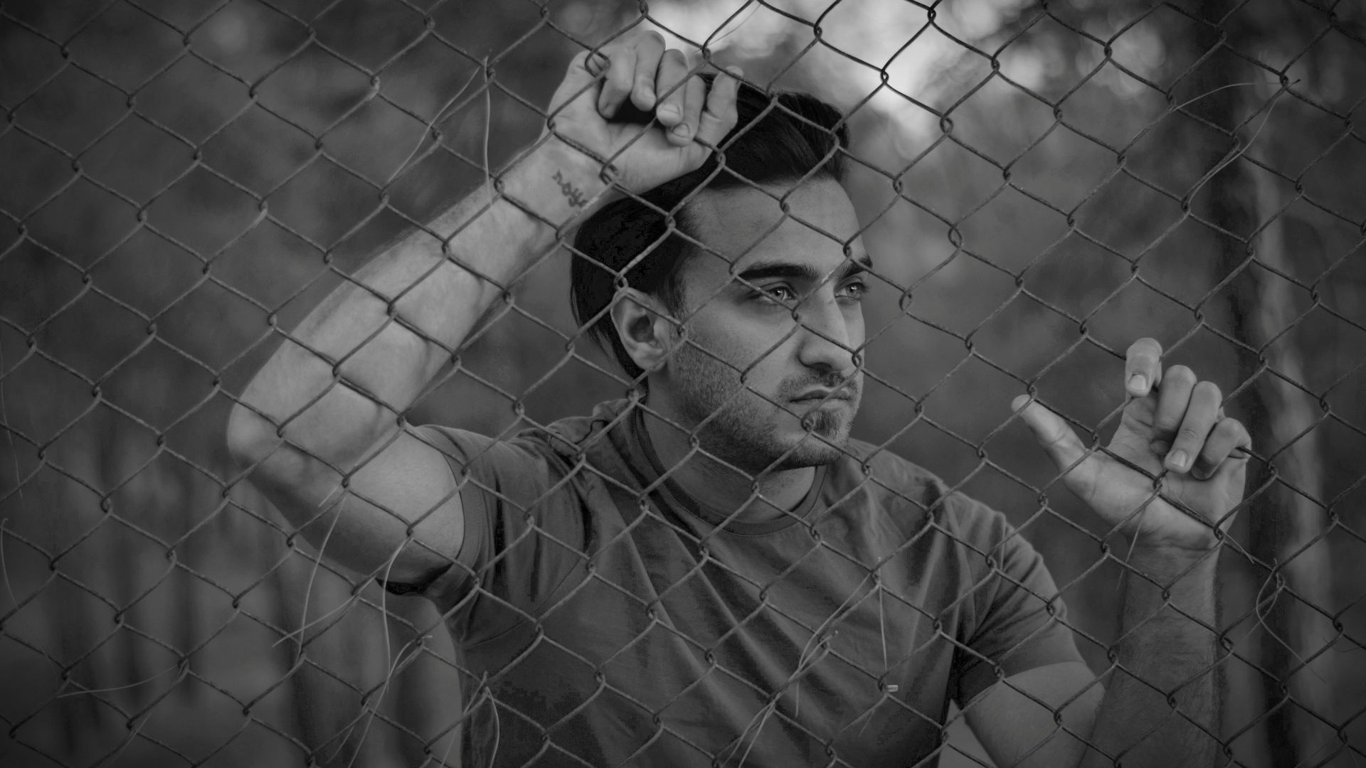 a man standing behind a fence holding a cigarette