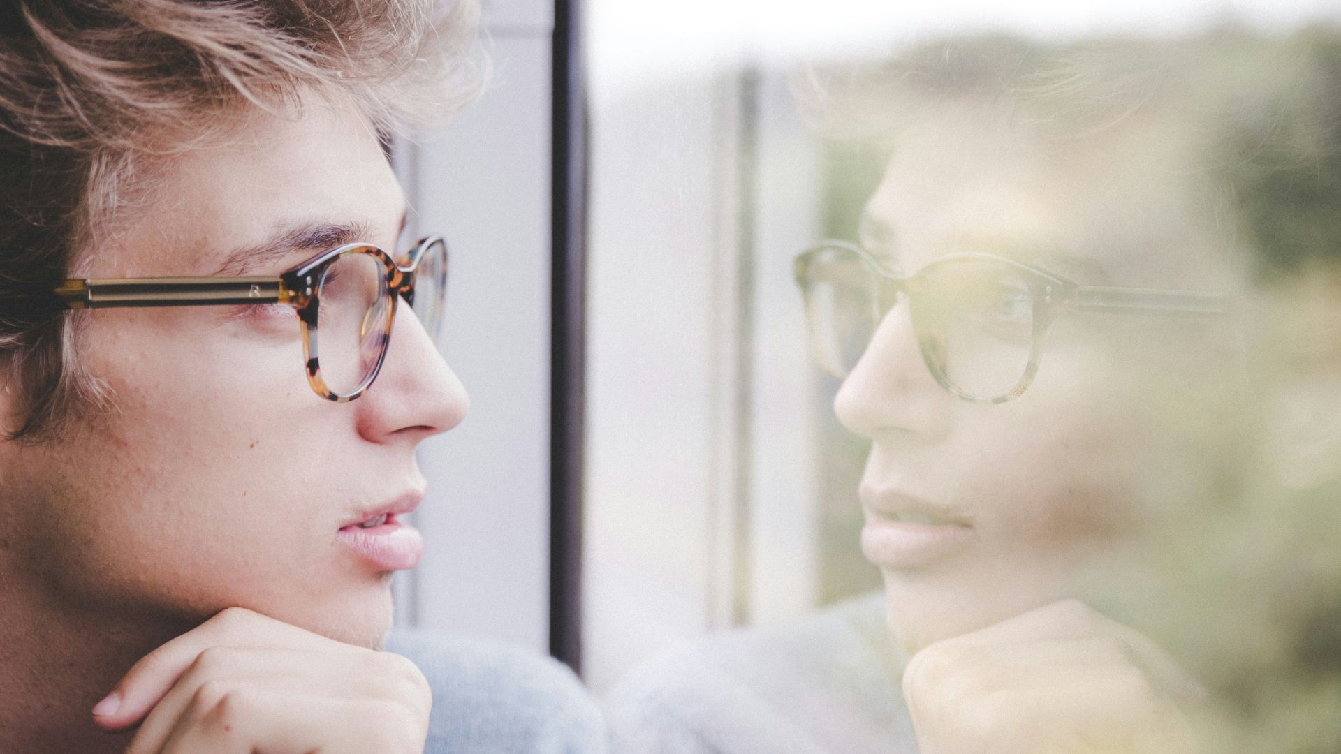 a man wearing glasses looking out a window
