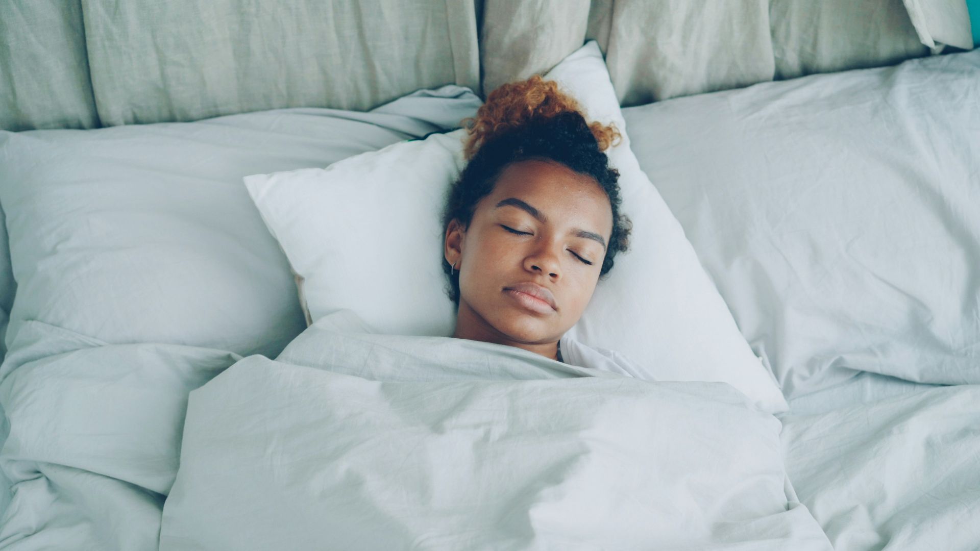 A young woman sleeping peacefully in a white bed.