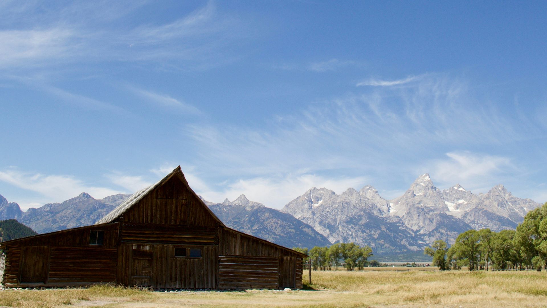 brown wooden house near snow covered mountain under blue sky during daytime