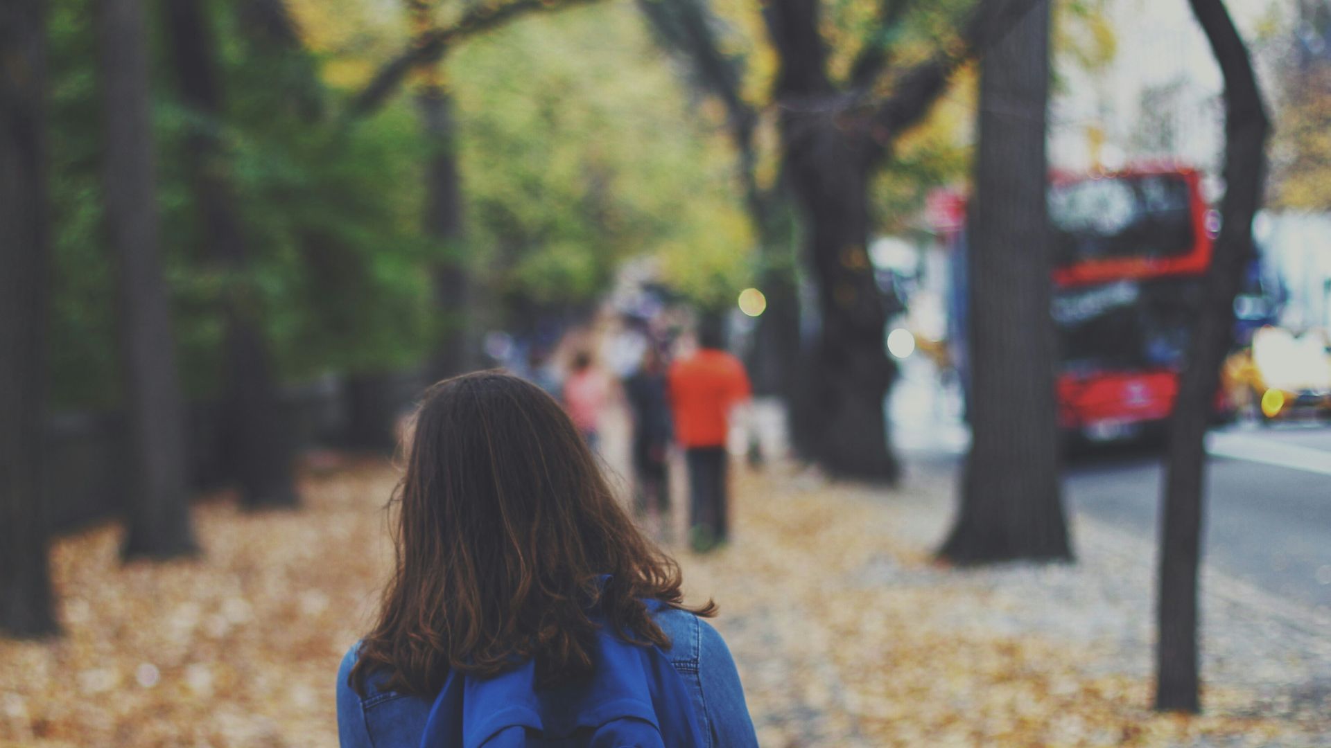 woman with blue backpack on street full of fallen leaves