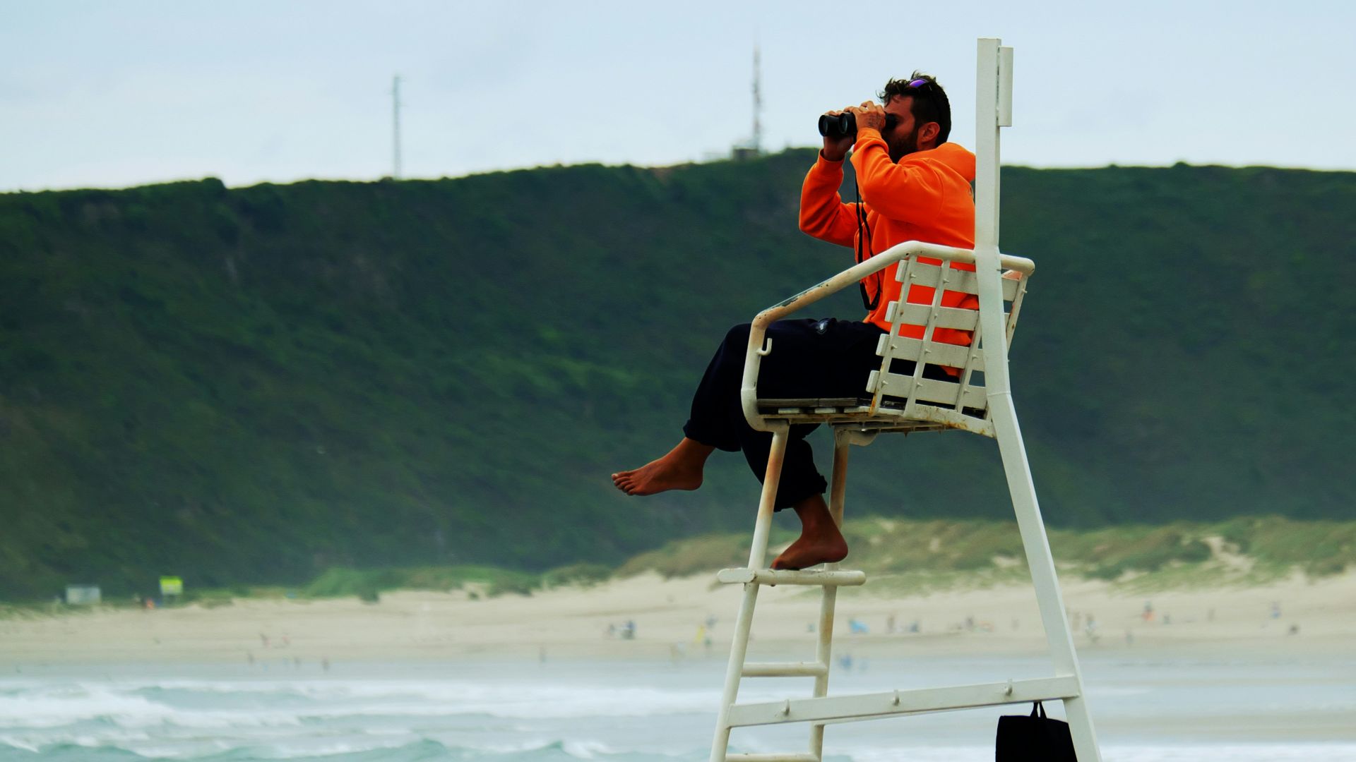 man in orange shirt sitting on white wooden folding chair on beach during daytime