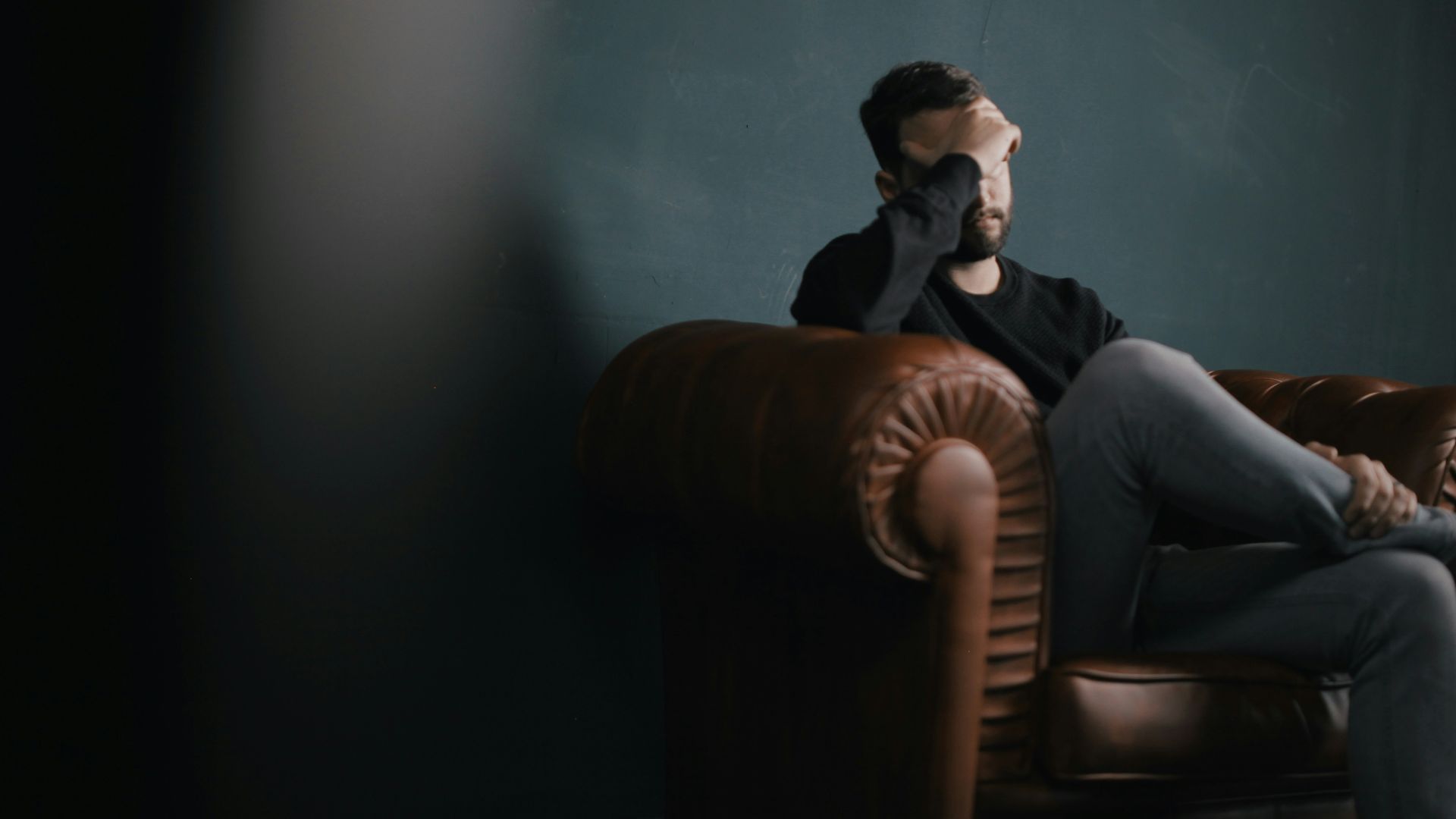 a man holds his head while sitting on a sofa