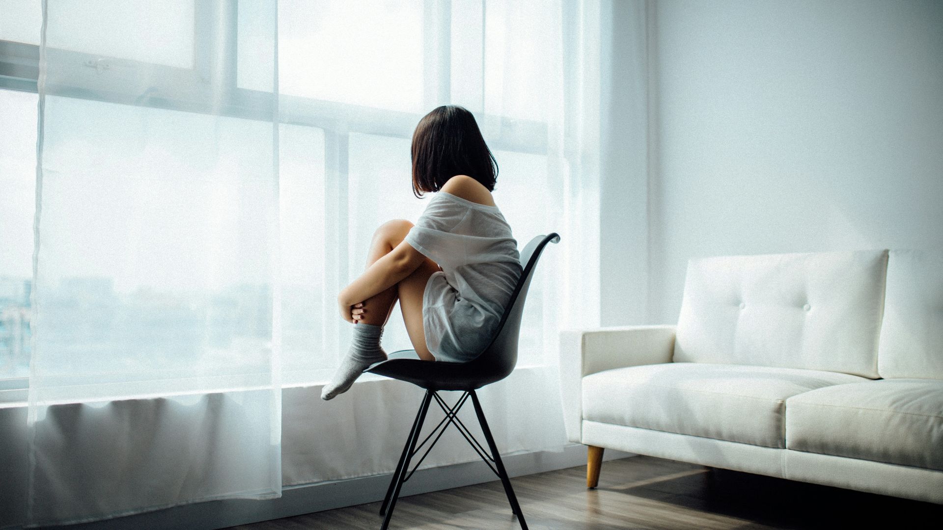 woman sitting on black chair in front of glass-panel window with white curtains
