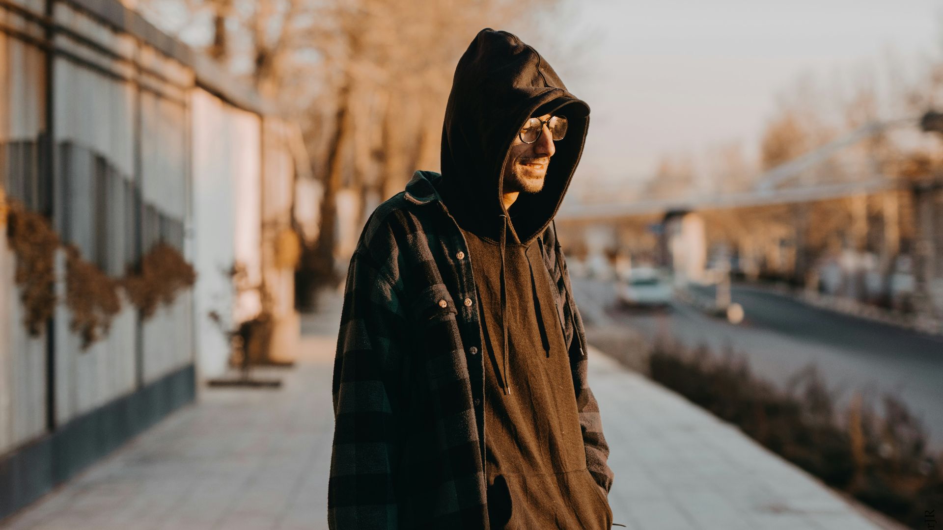 man in black and brown plaid hoodie standing on sidewalk during daytime