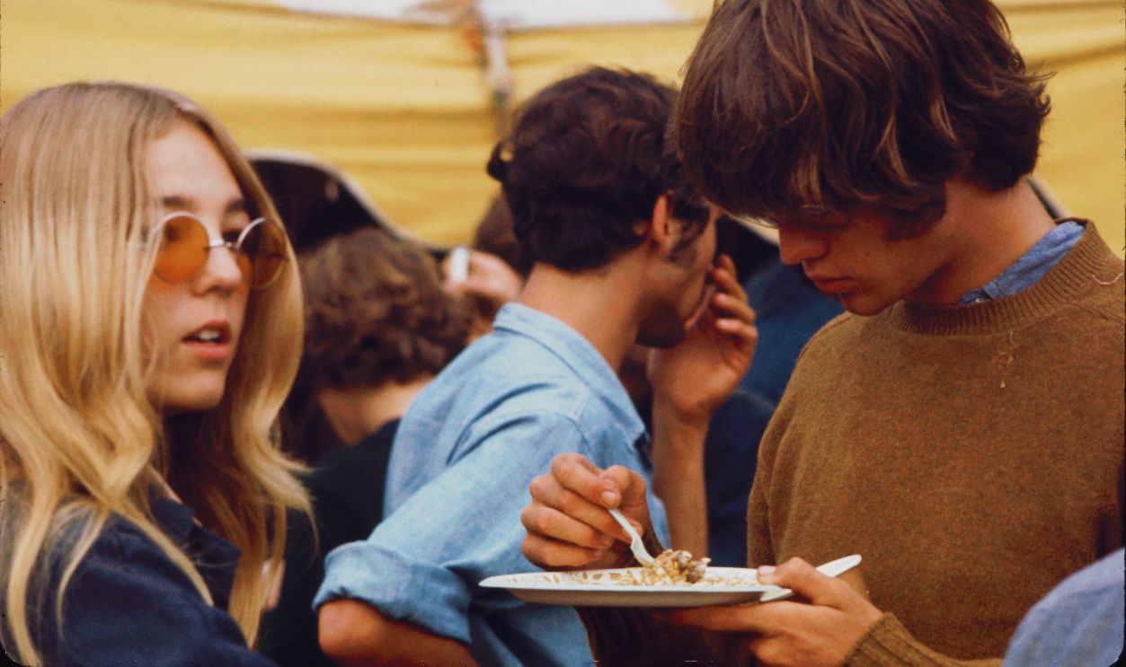 Gettyimages - 96243858, Food At Woodstock Standing with a young woman, a young man eats food from a paper plate outside a tent during the Woodstock Music and Arts Fair, Bethel, New York, August 1969. The food was prepared by the Hog Farmers, a group who had been asked to help construct, ensure security, and provide food for the event, Bethel, New York, August 1969. The festival ran from August 15 to 18.