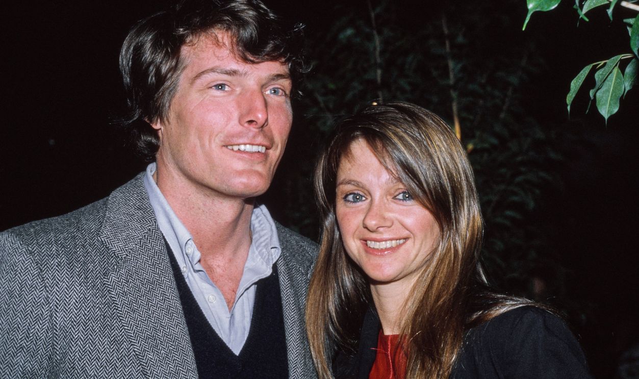 American actor Christopher Reeve, wearing a herringbone blazer over a light blue shirt and a black V-neck sweater, and his partner, British modelling executive Gae Exton, wearing a black coat over a red outfit, United States, circa 1983.