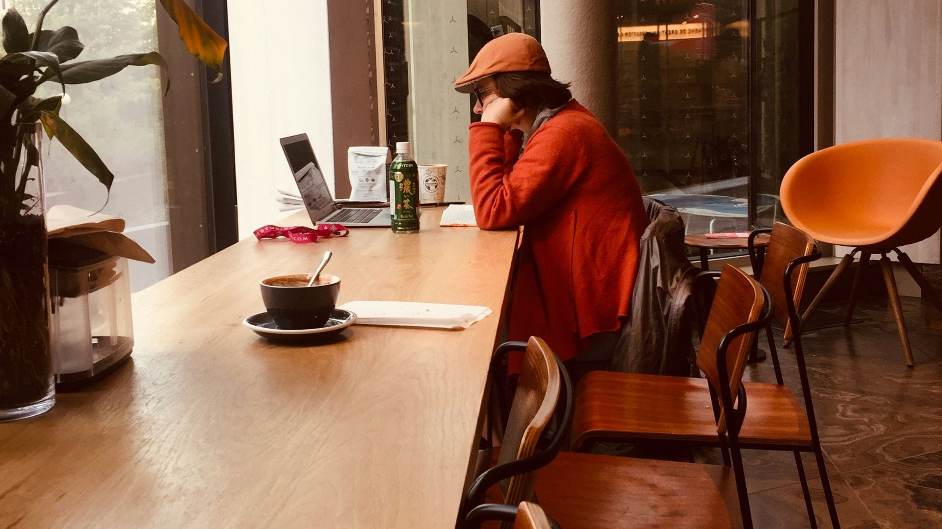 person wearing orange jacket sitting on chair while using laptop