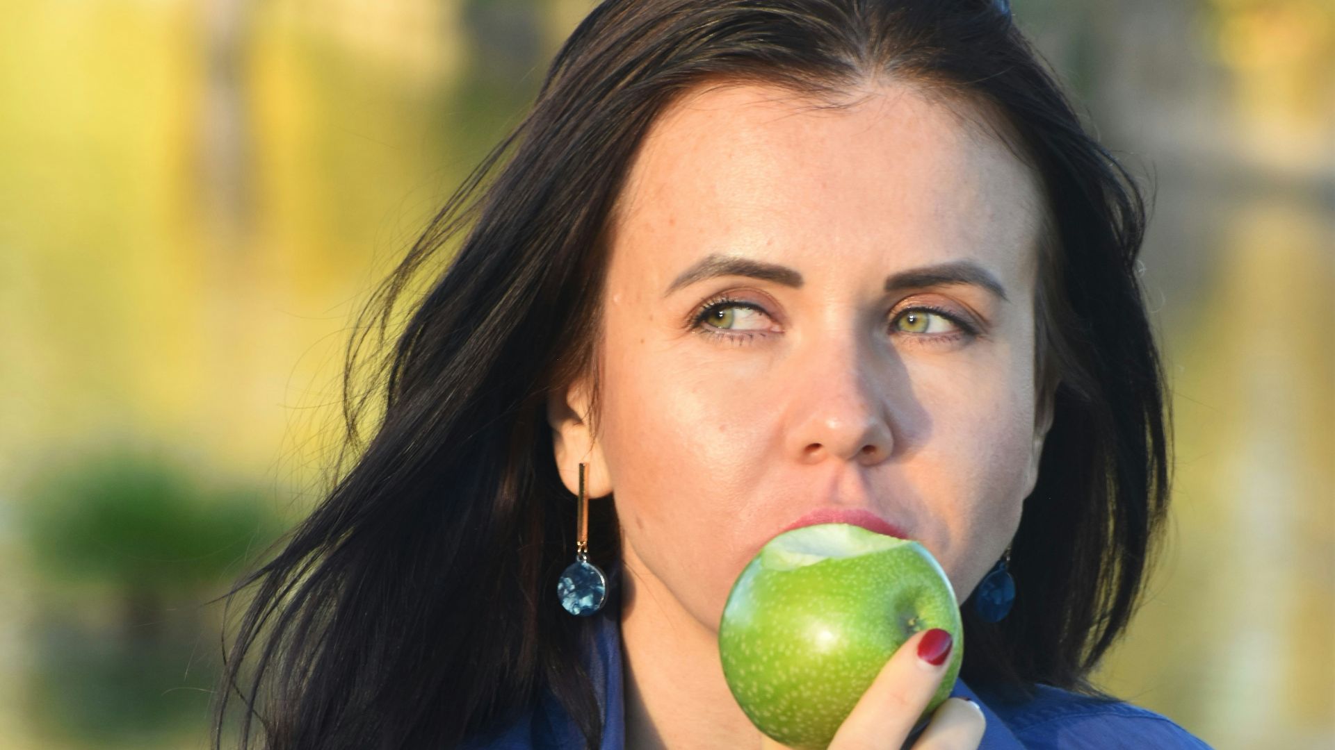 a woman in a blue shirt eating an apple