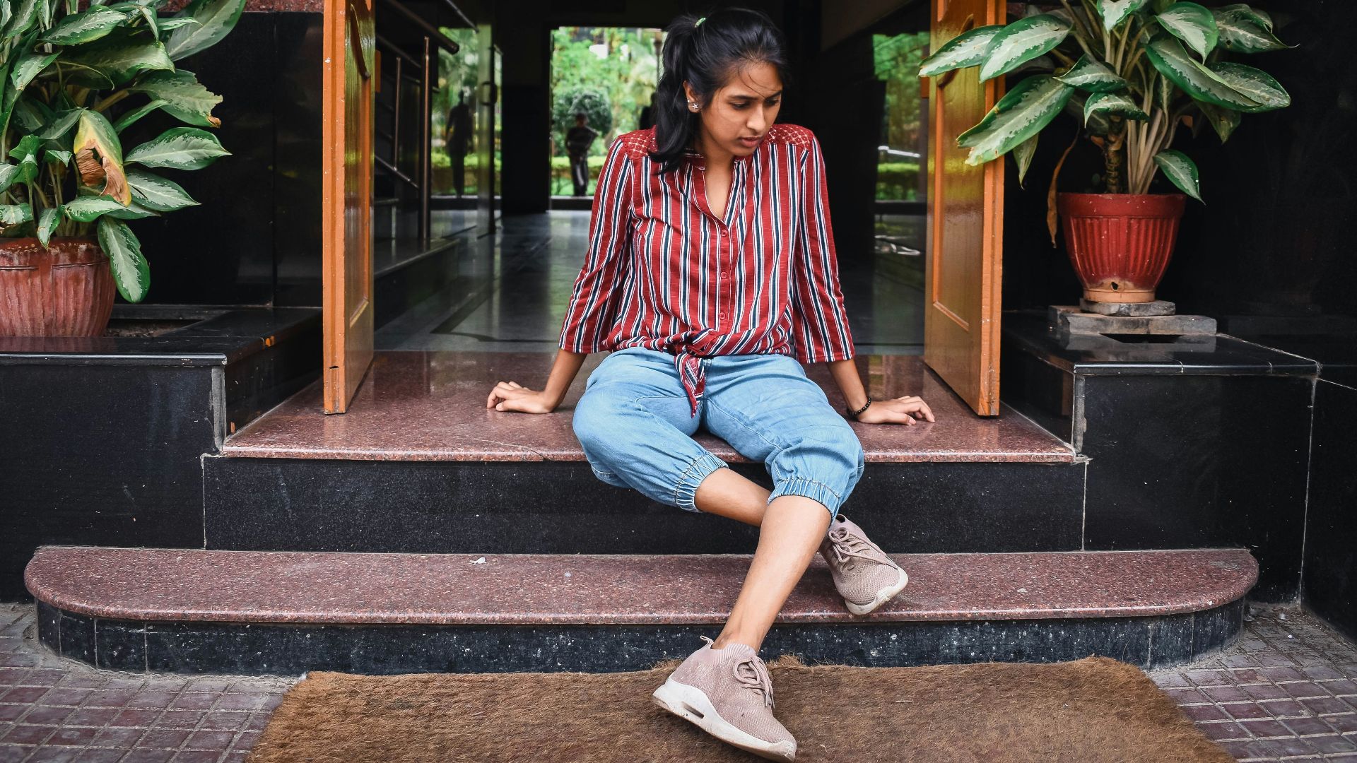 woman in pink and blue long sleeve shirt and blue denim jeans sitting on brown wooden