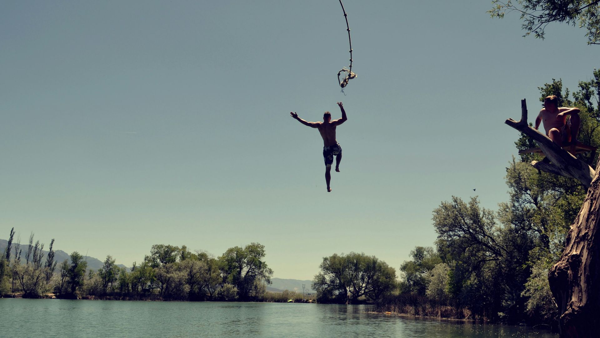man jumping on body of water with rope