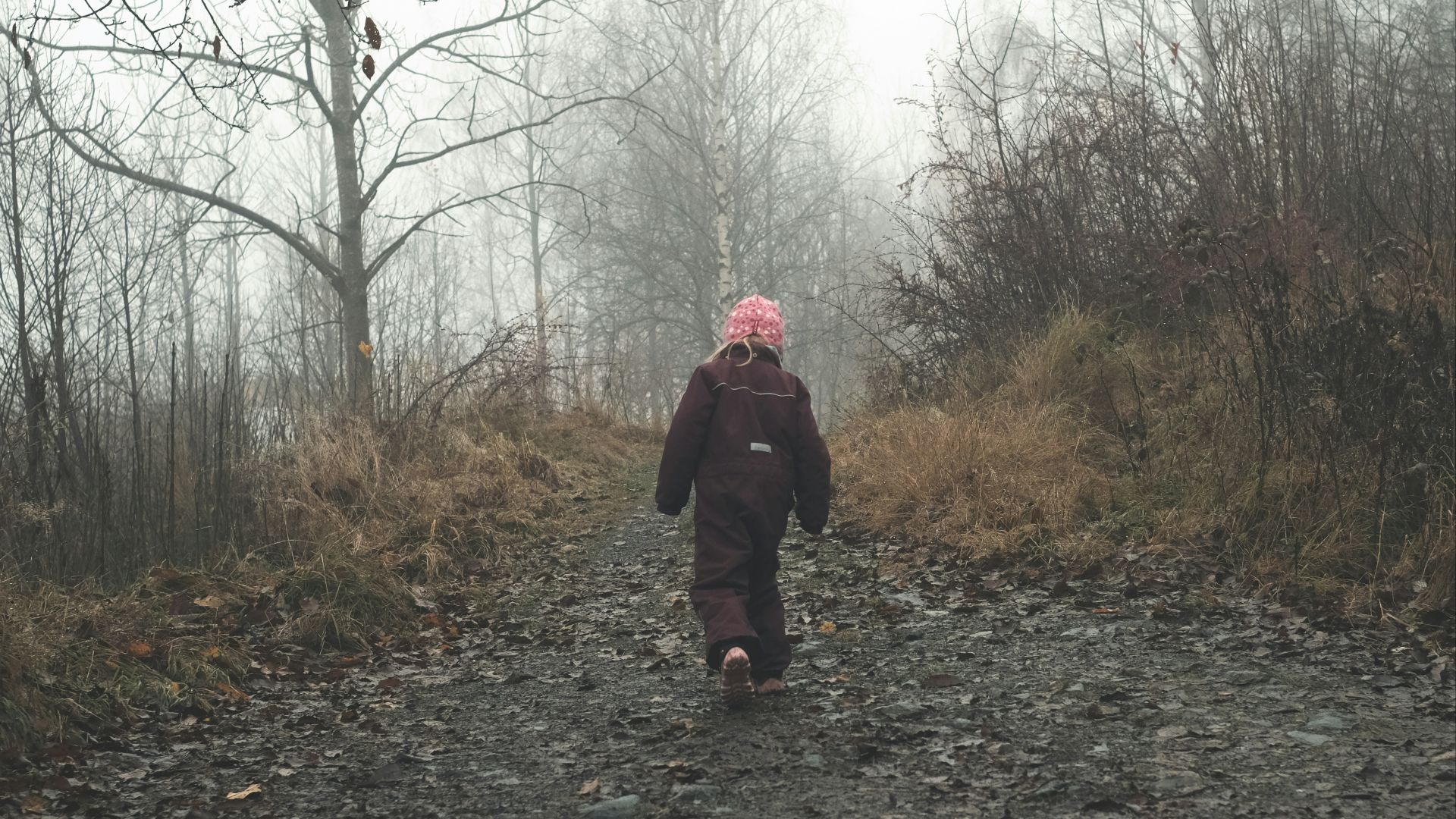woman in black jacket standing on pathway between bare trees